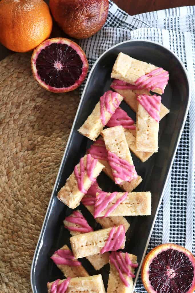 Almond Blood Orange Shortbread Cookies on a plate with sliced blood oranges.