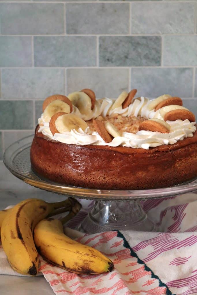Banana Pudding Cheesecake, on a cake stand with whole bananas underneath.